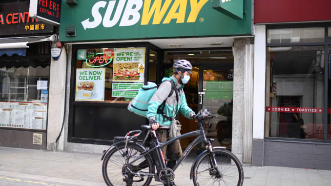 A delivery person wheels his bicycle outside a Subway shop.